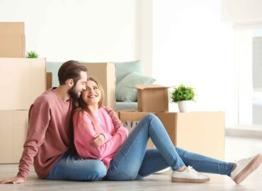 couple leaning against moving boxes while smiling