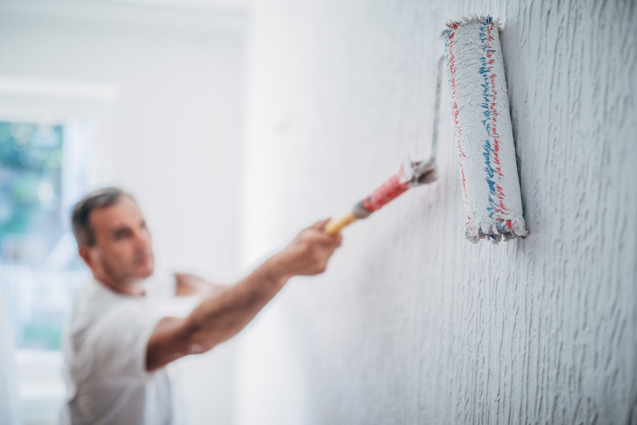 man paints the wall white with roller